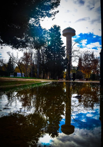 Imagen de un deposito de agua circular en altura, reflejado en un estanque de agua. 